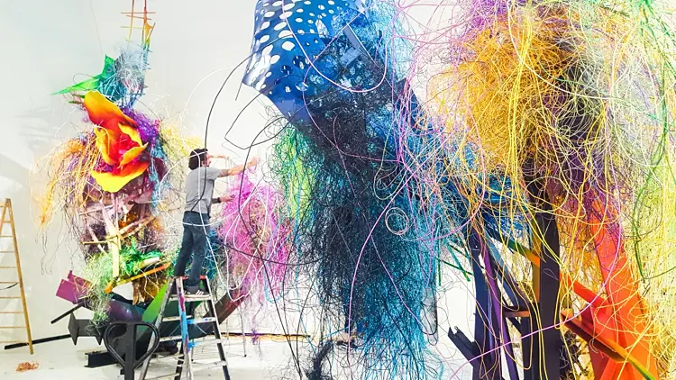A studio filled with towering sculptures made of bright, tangled strands and perforated blue forms.